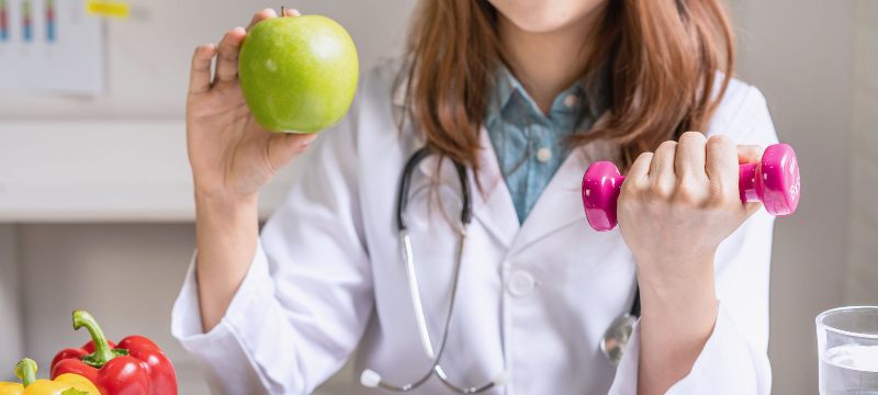 Médico sujetando una manzana y una pesa pequeña