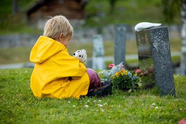 Niño con osito sentado ante la tumba de su madre