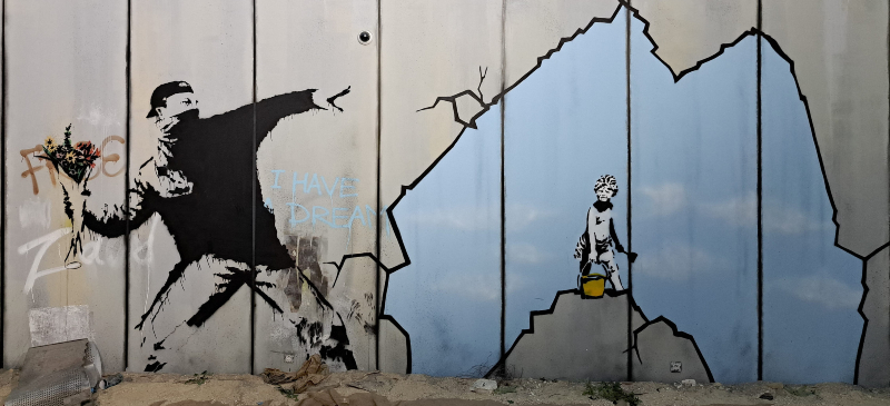 . Mural de un joven encapuchado con un ramo de flores para lanzarlo contra un niño en lo alto de una montaña