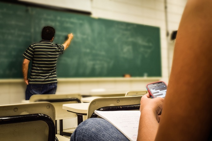 Un profesor escribe en la pizarra mientras un alumno manipula un móvil