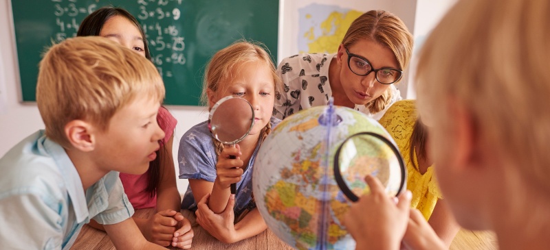 cómo enseñar geografía. Clase con la profesora y los alumnos alrededor de una bola del mundo. 