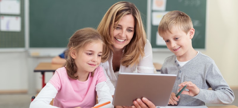 profesora con dos alumnos en una clase mirando un ordenador portátil