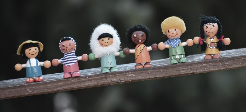 Diversidad. Muñecos de distintas razas del mundo dándose la mano sobre una pasarela de madera