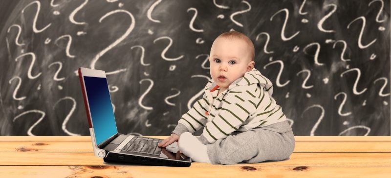 Bebé delante de un ordenador con una pantalla detrás llena de interrogantes