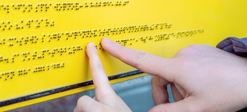Manos de niño y maestro leyendo un cartel en lenguaje braille