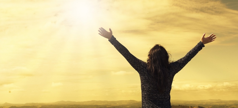 Mujer abriendo los brazos hacia el sol, metáfora de felicidad
