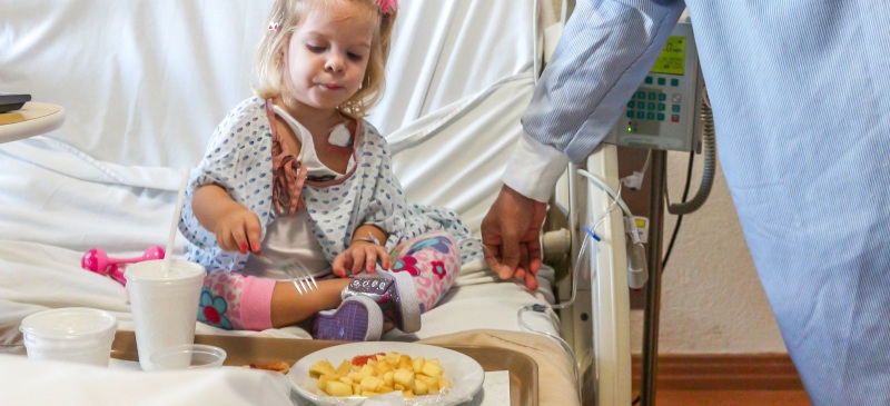 niña en el hospital comiendo sobre la cama un plazo de manzanas peladas