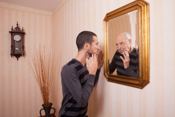 Hombre joven que se mira al espejo y se ve viejo