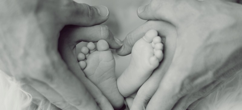 Imagen de pies de un bebé y las manos de sus padres rodeándolo haciendo un corazón
