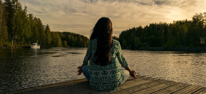 mujer haciendo yoga frente a un lago al amanecer