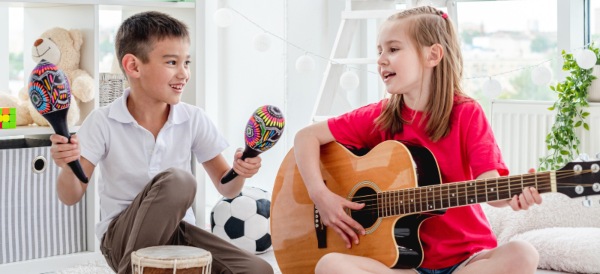 La música como método de aprendizaje. Dos niños cantando y tocando guitarra y maracas.