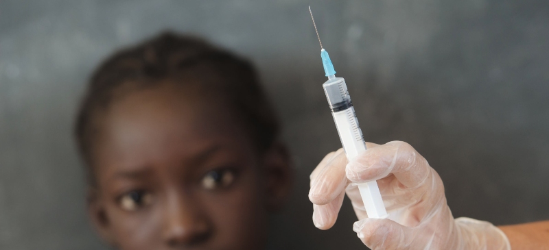 Imagen de una niña africana mirando una jeringuilla con una vacuna