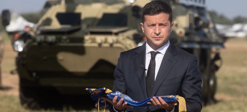 El presidente de Ucrania Zelenski con un tanque de fondo y una bandera en sus manos