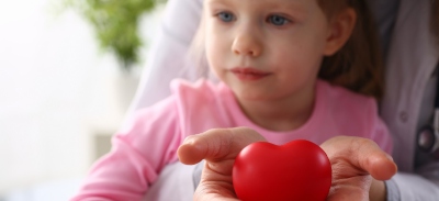Niña en los brazos de su médico acogiendo un corazón de juguete en las manos