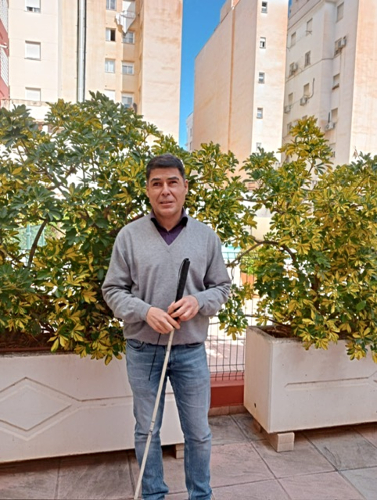 Carlos delante de unas macetas con bloques de edificios al fondo