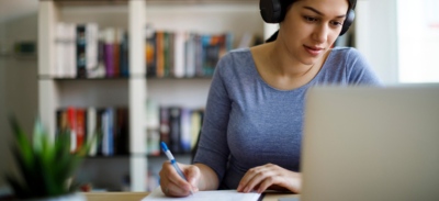 Chica estudiando un examen con cascos en su casa, preparando las oposiciones de Correos
