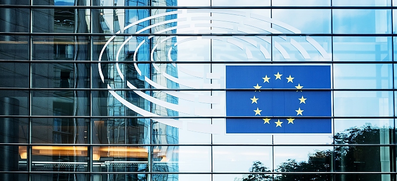 Fotografía del exterior del Parlamento Europeo con la imagen de la bandera de la Unión Europea reflejada en la cristalera.